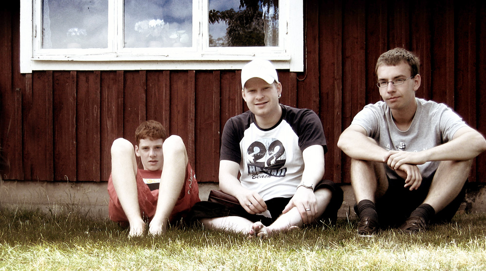 drei Jugendliche sitzen vor einem Holzhaus