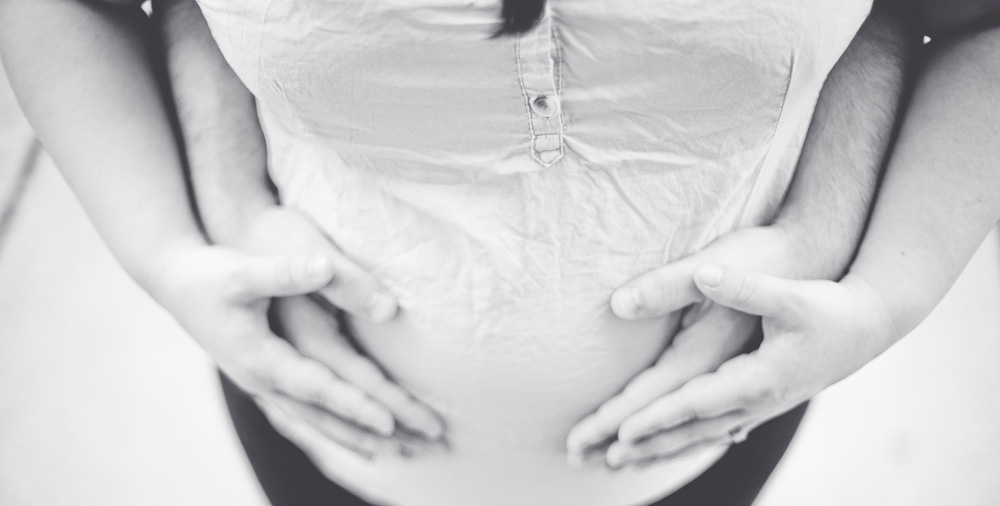 4 Hände liegen auf einem schwangeren Bauch