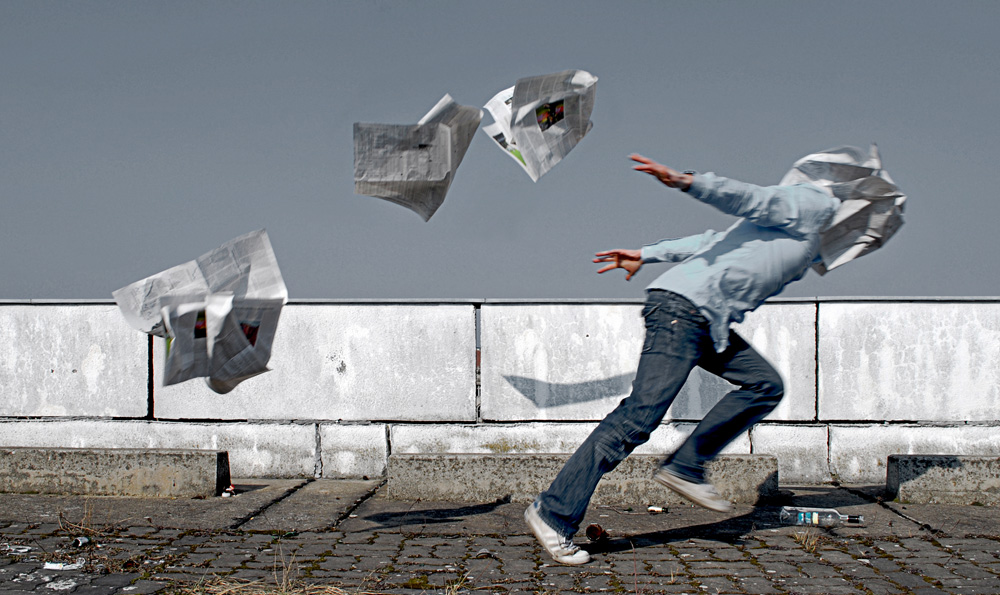 ein Mann kämpft gegen fliegende Zeitungen an